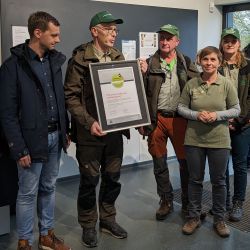 Uwe Müller hält das neue Faltblatt, Claudia Wilhelm und Martin Kozber die Förderplakette in den Händen